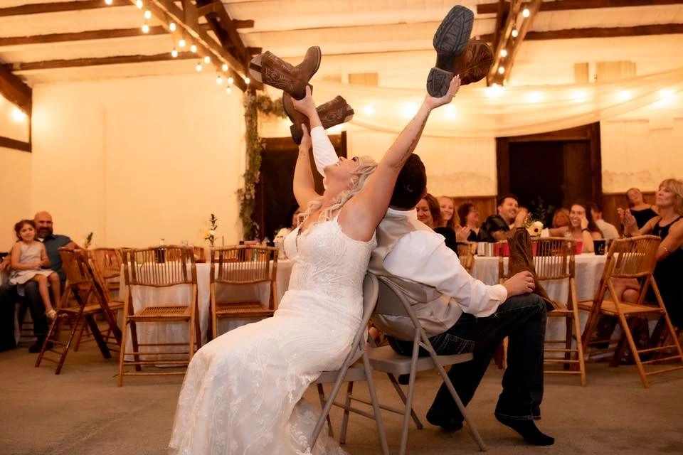 A bride and groom playing the wedding shoe game with cowboy boots in the rustic reception barn at Stone Ridge Estates in Pasco, WA.