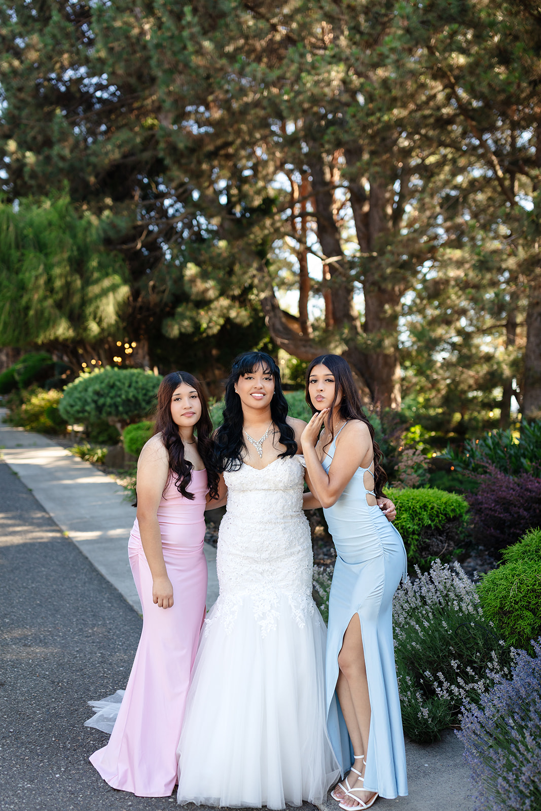 Bride with two loved ones in the garden beneath the evergreens