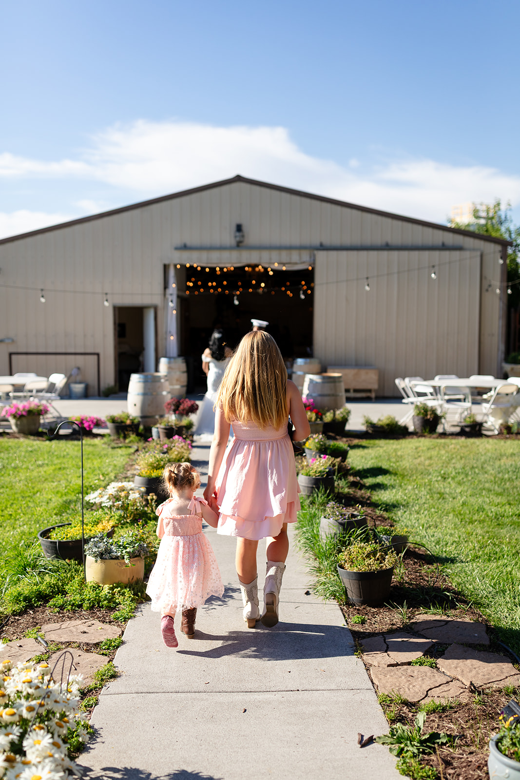 Two flower girls walking through the gardens toward the reception barn