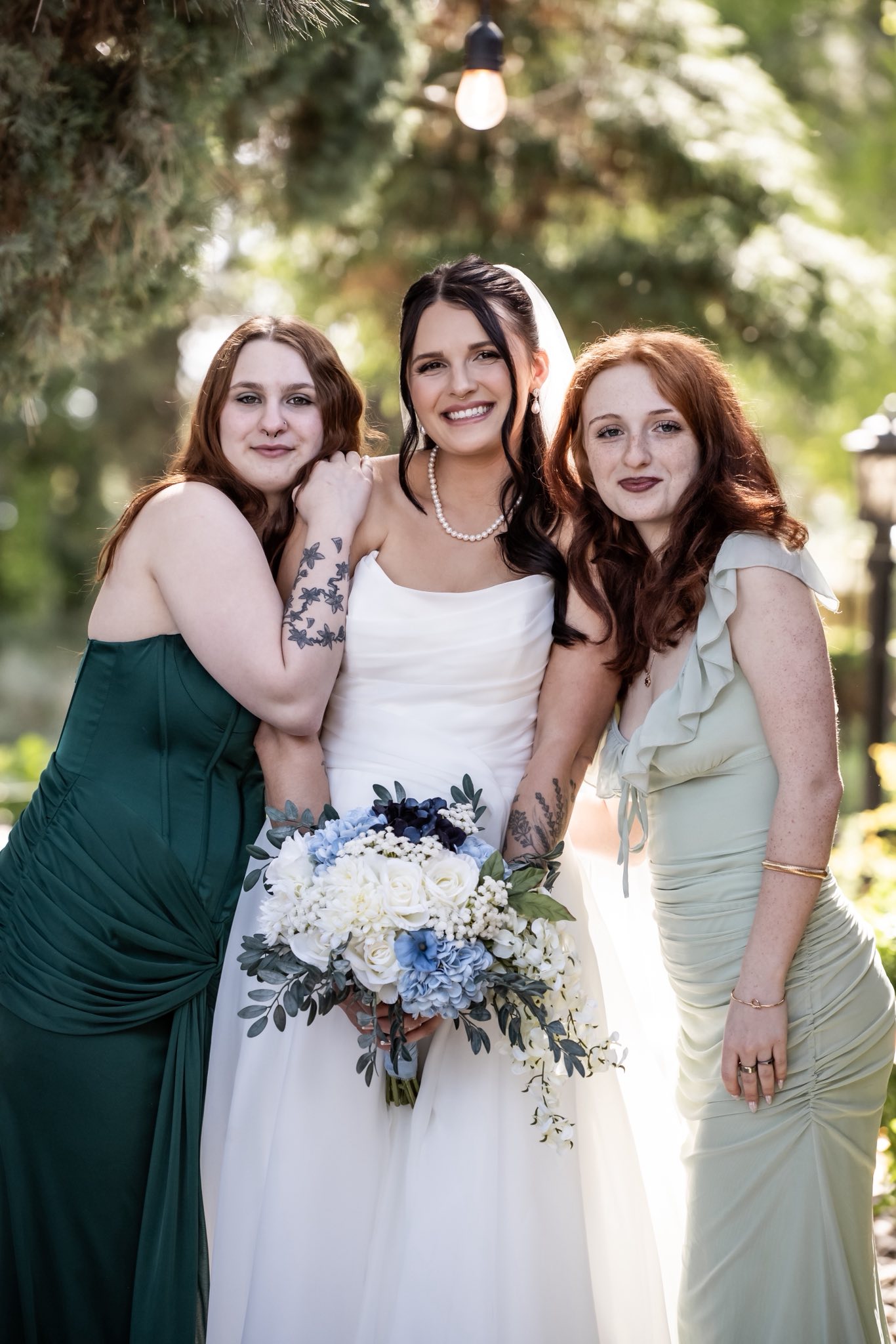 A bride sharing a portrait with two of her favorite people beneath the trees