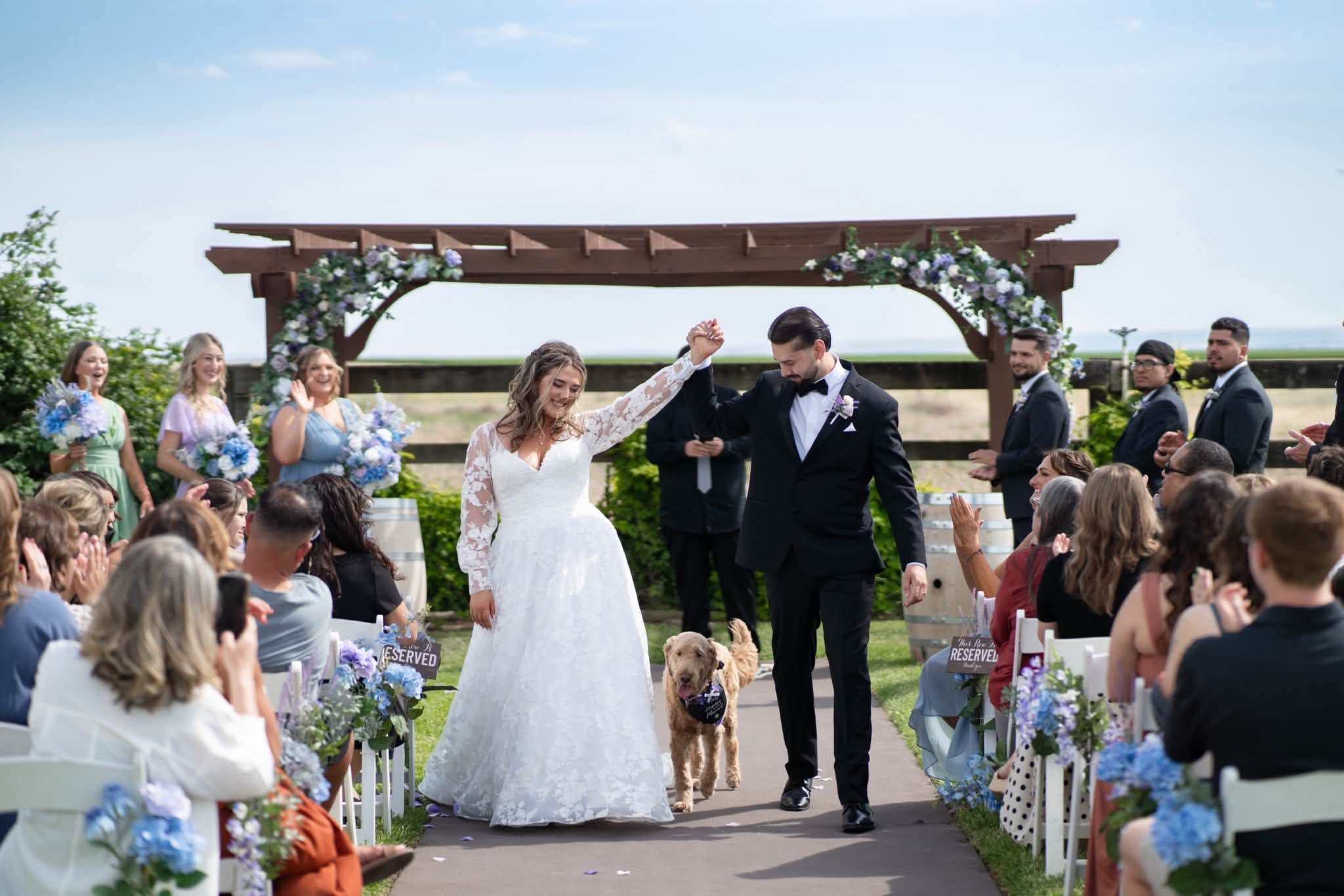 Newlyweds and their dog walking back up the outdoor ceremony aisle