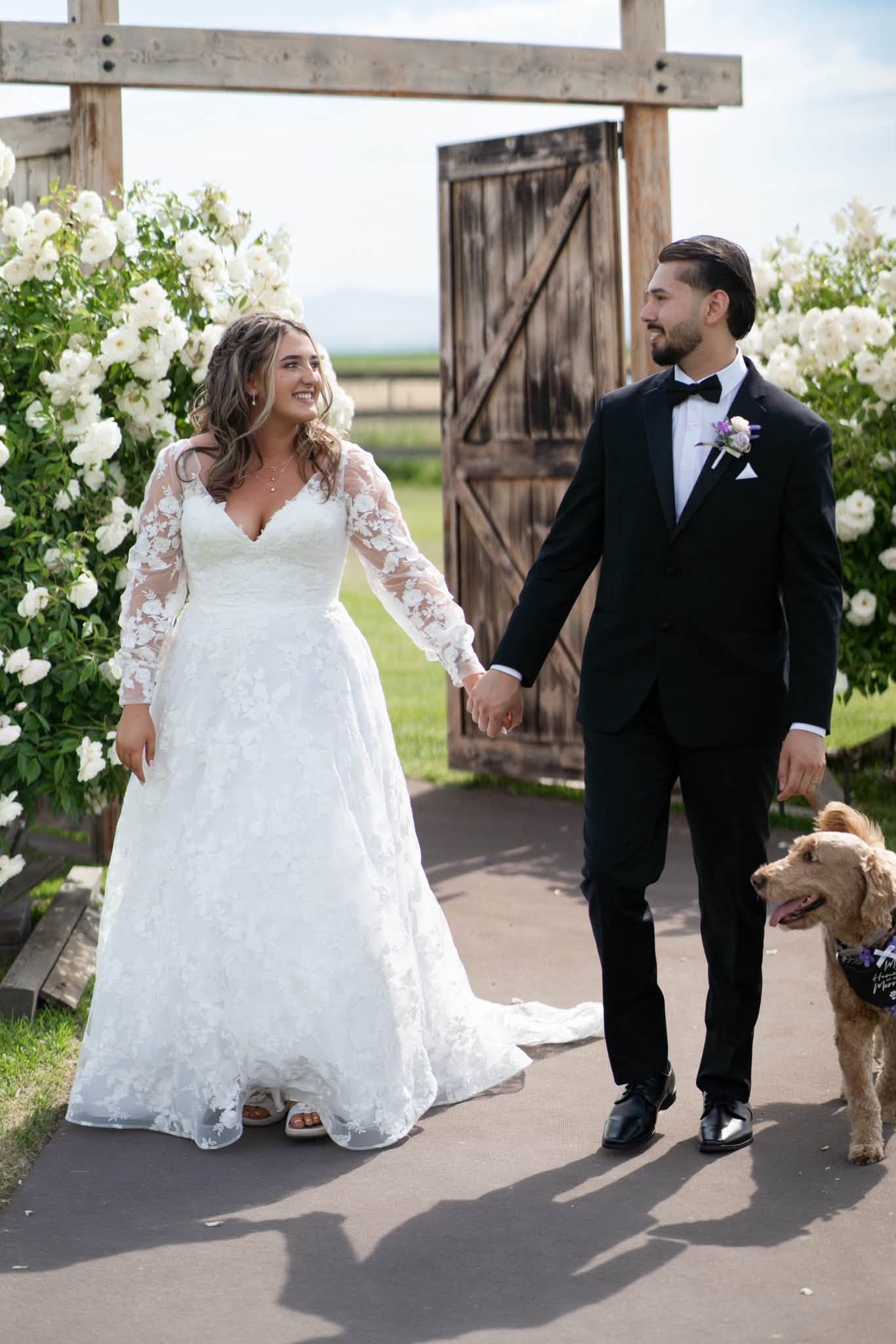 A newly married couple and their dog beneath the flower-covered ceremony arbor